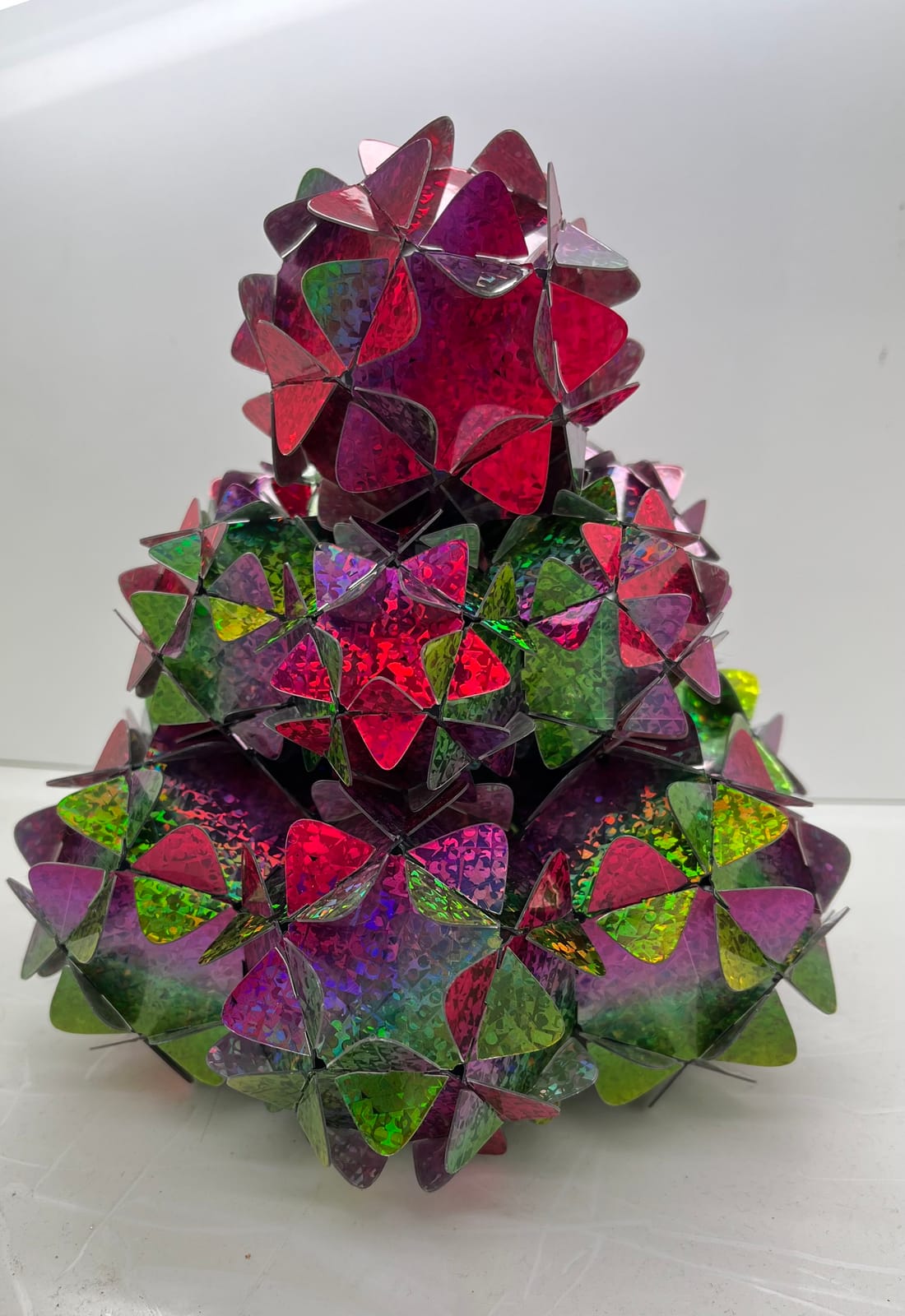 Sapin construit en trois étages de pièces holographiques roses, rouges et vertes