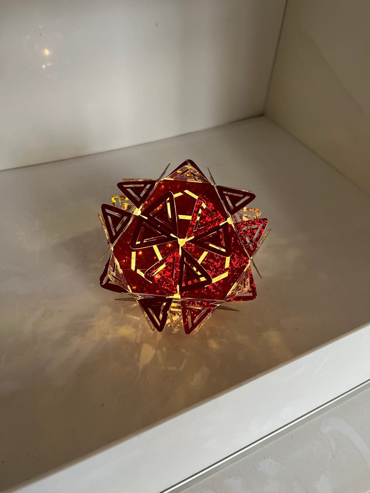 Étoile en pièces rouges holographiques, allumée, posée sur une étagère